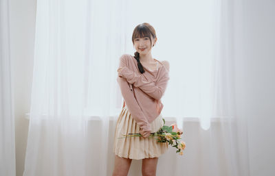 Portrait of young woman standing against wall