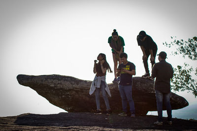 People standing on rock against clear sky