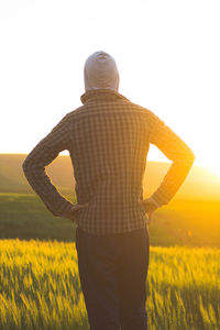 Rear view of man standing on farm against sky during sunset