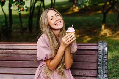 Smiling young woman in a pink dress holding a cupcake with pink frosting and candle