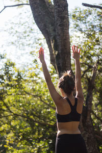 Rear view of teenage girl with arms raised standing against trees in park