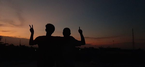 Rear view of silhouette people standing against sky during sunset