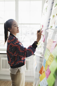 Businesswoman writing in adhesive note on whiteboard at office