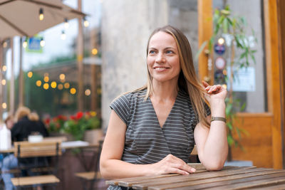 Confident young woman sitting in a street cafe at a table in a gray striped