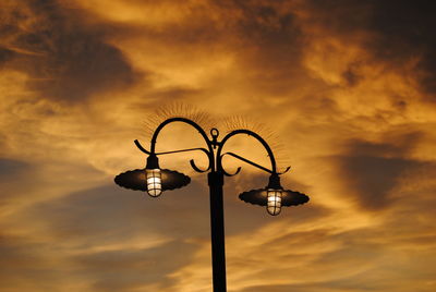 Low angle view of illuminated street light against cloudy sky at sunset