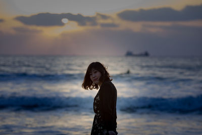 Young woman standing at beach during sunset