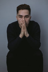 Portrait of young man sitting against wall