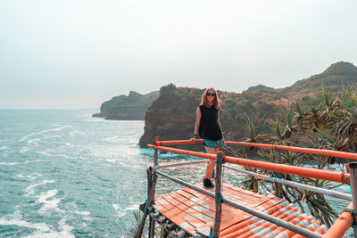 Full length of woman standing at observation point by sea against sky
