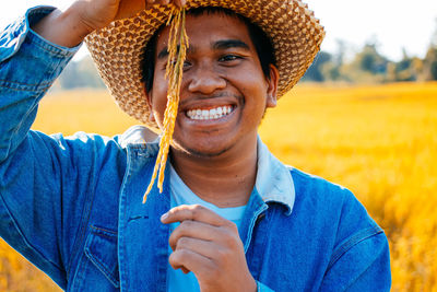 Portrait of smiling man wearing hat while holding cereal plant on field 