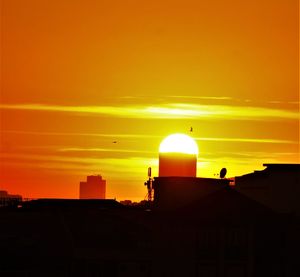 Silhouette buildings against orange sky during sunset