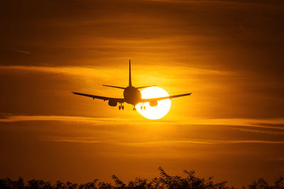 Low angle view of silhouette airplane against orange sky