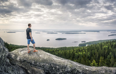 Man standing on rock by sea against sky