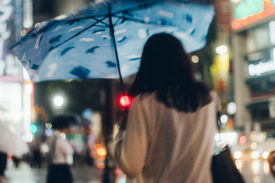 Rear view of woman with umbrella walking at night