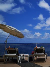 Deck chairs on beach against sky