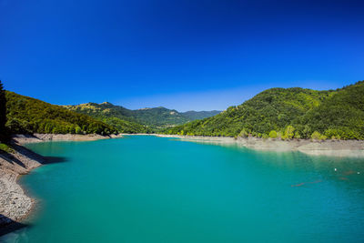 Scenic view of lake by mountains against clear blue sky