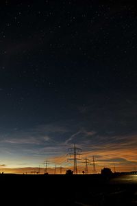 Silhouette electricity pylons field against sky at night