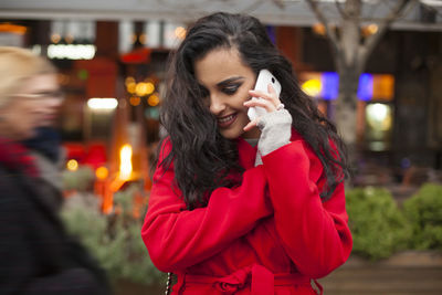 Smiling young woman talking on mobile phone while standing on city street