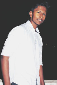 Portrait of young man standing against black background