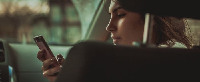 Young woman holding smart phone in car