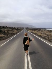 Rear view of woman hitchhiking on road against sky