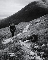 Rear view of hiker walking on trail by mountain against sky