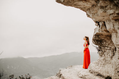 Woman with red cloth standing on rock against clear sky