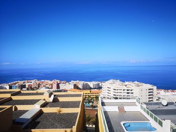 High angle view of buildings by sea against blue sky