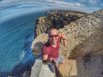 Portrait of smiling young man holding monopod against sea