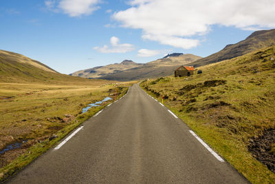 Empty road leading towards mountains against sky