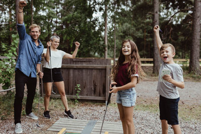 Cheerful family with arms raised playing miniature golf in backyard
