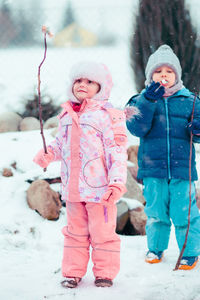 Full length of cute siblings eating marshmallow while standing on snow covered field