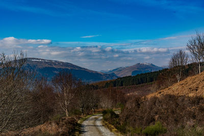 Road leading towards mountains against blue sky