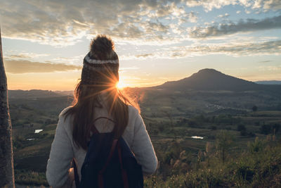 Rear view of woman looking at landscape against sky during sunset