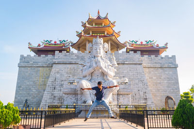 Portrait of man with arms outstretched standing against buddhist temple