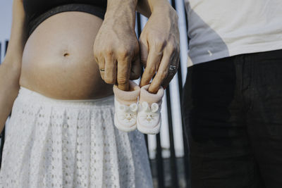 Midsection of man and pregnant woman holding baby booties while standing at home