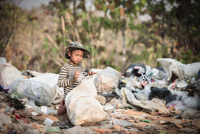 Cute boy sitting by garbage outdoors