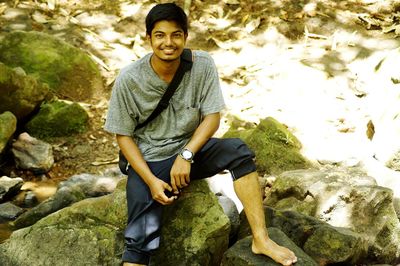 Portrait of young man sitting on rock against trees