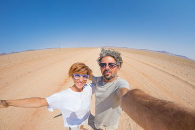 Portrait of young couple standing in desert against clear blue sky