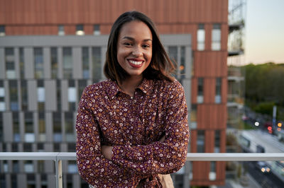 Happy young woman with arms crossed in balcony