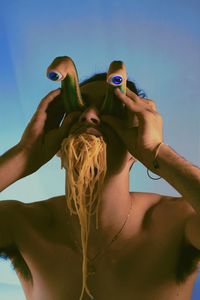 Low angle view of man holding artificial eyes while noodles in mouth against sky