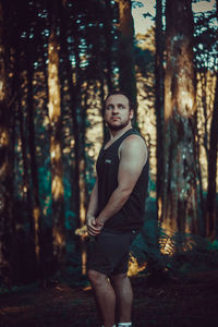 Portrait of young man standing against trees in forest