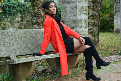 Side view of young woman sitting against trees