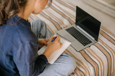 Midsection of woman writing on notepad at home