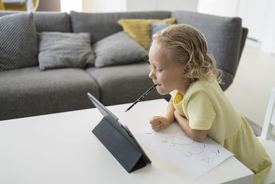 Girl with pencil in mouth leaning on table at home