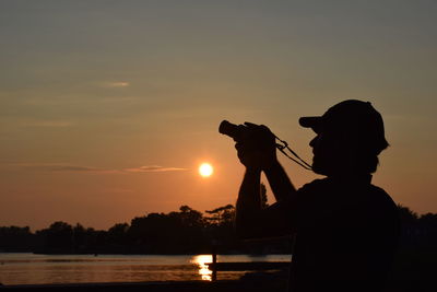 Silhouette man photographing at sunset