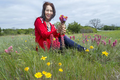 Beautiful young woman standing by yellow flowers on field