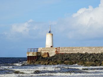 Lighthouse by sea against sky