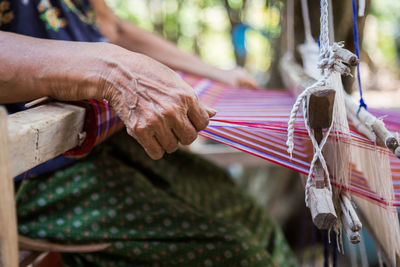 Midsection of woman weaving thread in loom