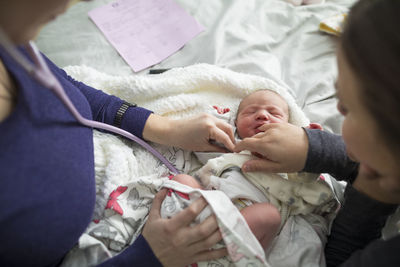 High angle view of midwife examining newborn baby girl by woman on bed at home