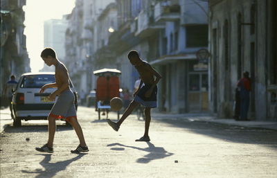 Shirtless boys playing soccer on street in city